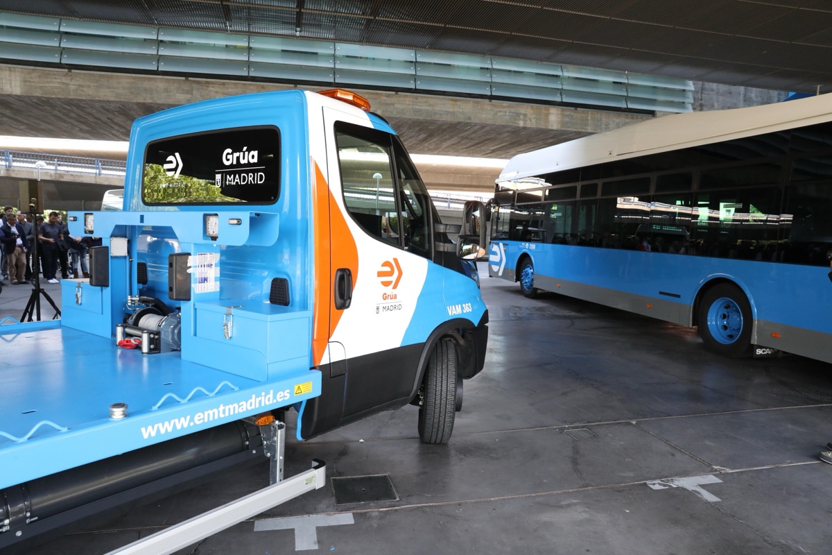 Grúa municipal de Madrid de color azul con el rótulo «Grúa Madrid», junto a un autobús de la EMT